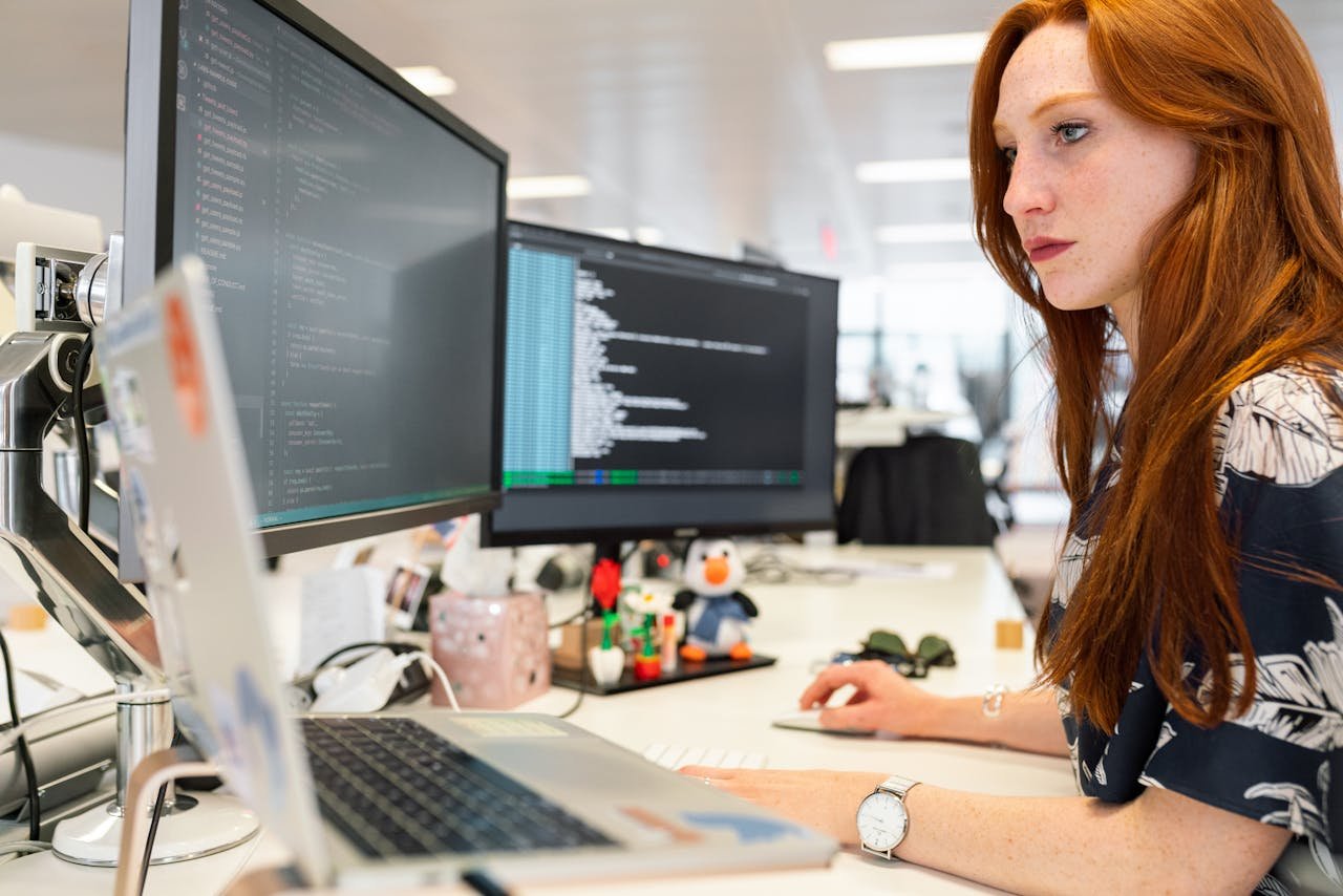 A SEO Specialist woman with red hair focused on her computer screen, typing diligently.