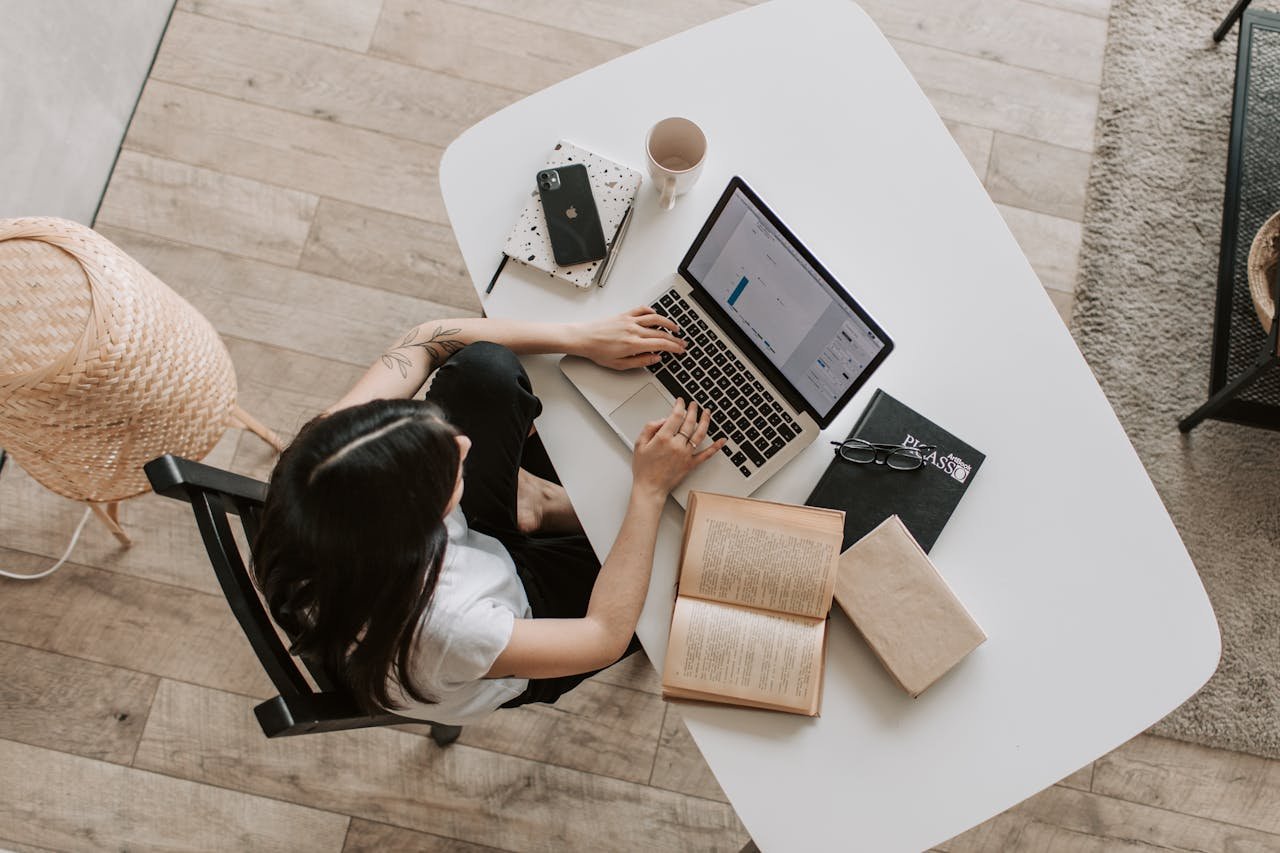 A woman at a table with a laptop and books, working as an SEO specialist to optimize a website.